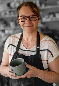 the hands behind the clay showing the maker in her studio wearing apron and holding a pot