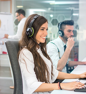 Young positive woman customer support phone operator in microphone headset working on comp