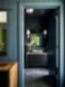 Stylish bathroom with black vanity, stone sink, and floral decor. Dark walls and floor; green door visible. Warm, elegant ambiance. on HomeFindss by STEVE & FILIP DESIGN