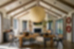 Cozy living room with vaulted ceiling, wooden beams, and a large paper lantern. Fireplace with stacked wood, and a rustic dining table. on HomeFindss by STEVE & FILIP DESIGN