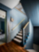 Blue paneled staircase with beige carpet, wooden handrails, and a decorative wreath. Wooden floor and adjacent room visible. Calm, stylish ambiance. on HomeFindss by STEVE & FILIP DESIGN