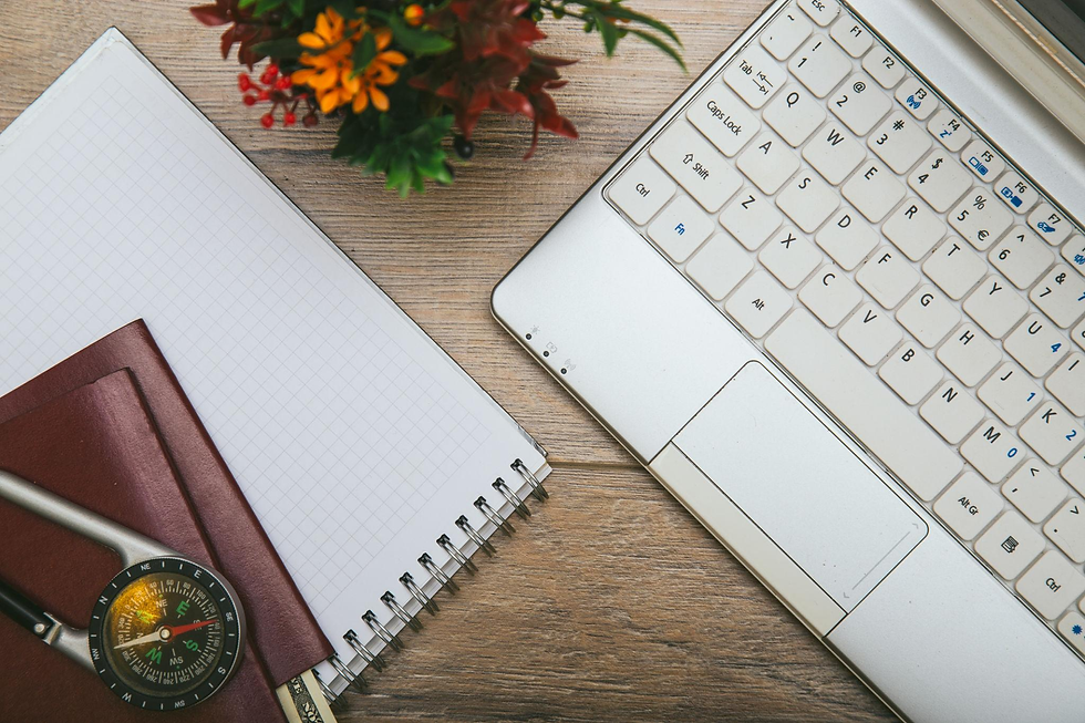 Laptop keyboard on wooden desk with a grid notebook, a pen, a compass, and a colorful potted plant. Bright and organized setting. MICHELLE DANNER ACTING SCHOOL 
