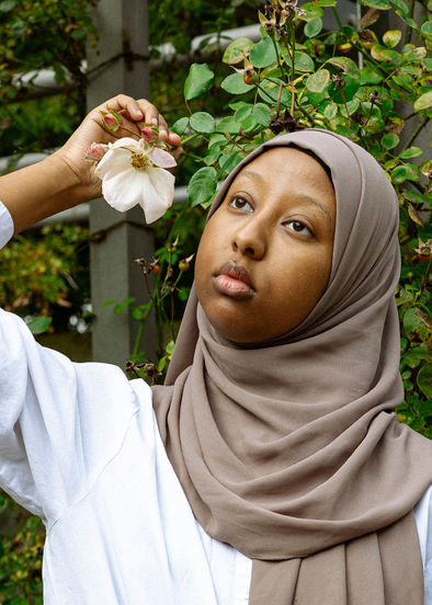 Foto von Maymuna, die verträumt in die Gegend schaut und eine Rose neben ihrem Gesicht hält