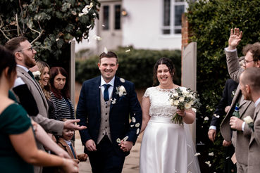 Just married couple walking through rose petal confetti at Houchins Essex