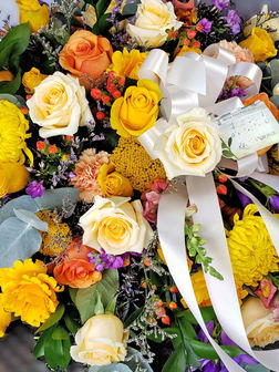 Funeral casket spray floral arrangement with yellow, orange, purple and cream flowers with greenery and berries