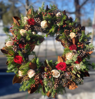 Funeral floral wreath arrangement of red and champagne roses with greenery, pinecones, and berries