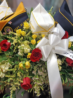 Funeral casket spray floral arrangement with shades of cream, yellow and red flowers with greenery and uniform hats