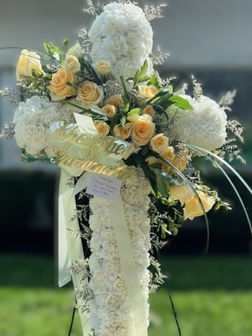Funeral floral cross made of white flowers sashed with pale yellow roses