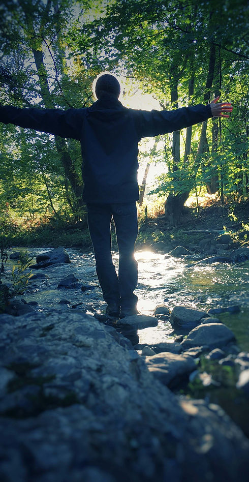 Mann seht mit ausgebreiteten Armen auf Stein im Fluss