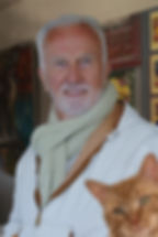 Head shot of David Lewis, who has white hair and a beard and is wearing a zippered white jacket and a scarf around his neck. Hank, a marmalade cat, has photo-bombed the picture.