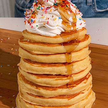 Una torre di pancake con panna montata, codette e sciroppo d'acero