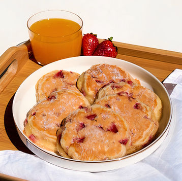 Morbidi pancake alle fragole disposti a cerchio, con zucchero e spremuta d'arancia