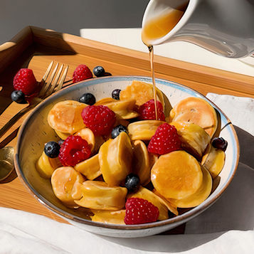 Una ciotola con mini pancake alla banana, con frutti di bosco freschi e sciroppo d'acero