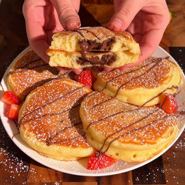 Cinque pancake ripieni di Nutella disposti a cerchio, con fragole e zucchero a velo. Ricetta di Pancake Eden