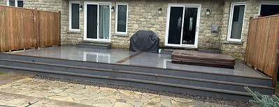 Ground-level composite deck with stone patio and privacy fence – custom backyard build