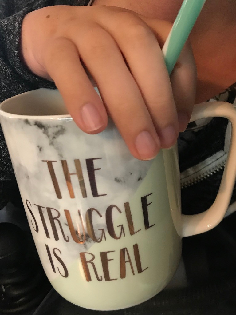ID: Cristina with her hand on a mint and marble mug while holding a mint straw. The mug has the words "the struggle is real" on it with gold foil.