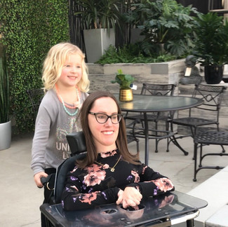 A woman giving a child a ride on the woman’s wheelchair while they explore a greenhouse 