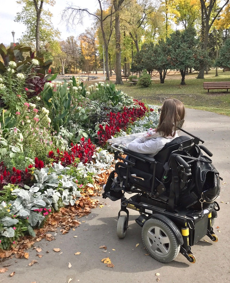 Cristina Waldner, a girl with SMA in wheelchair, looking at flowers at St. Vital Park in Winnipeg, Manitoba, Canada.