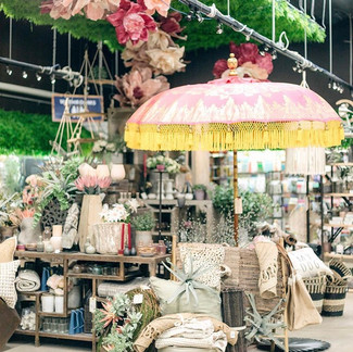 Shop display with tropical decor, a parasol, and a flower installation