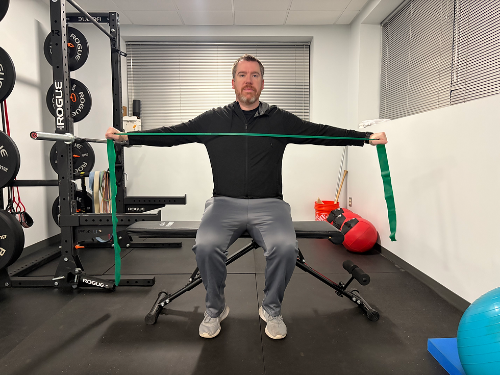 Man sitting on weight bench and stretching a green band out to both sides, performing a horizontal abduction