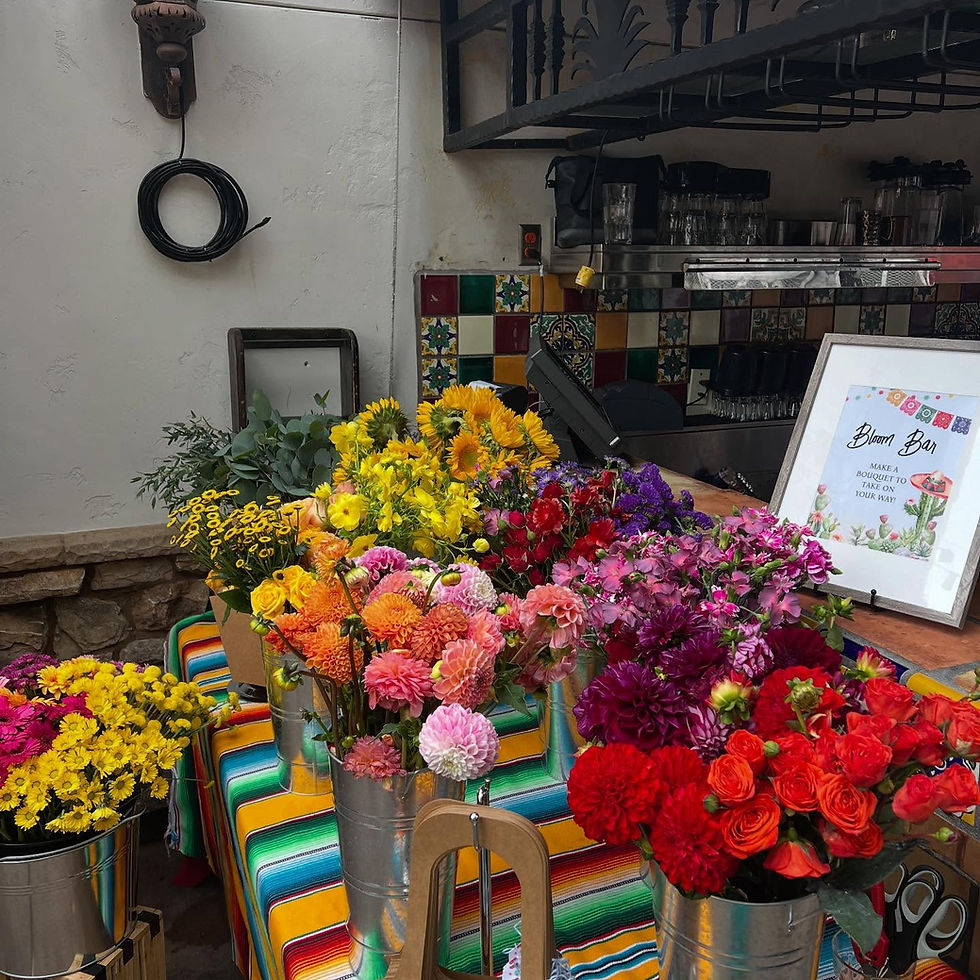 Colorful bloom bar display with buckets of fresh flowers in red, yellow, pink, and purple, set on a striped tablecloth for a festive floral celebration.