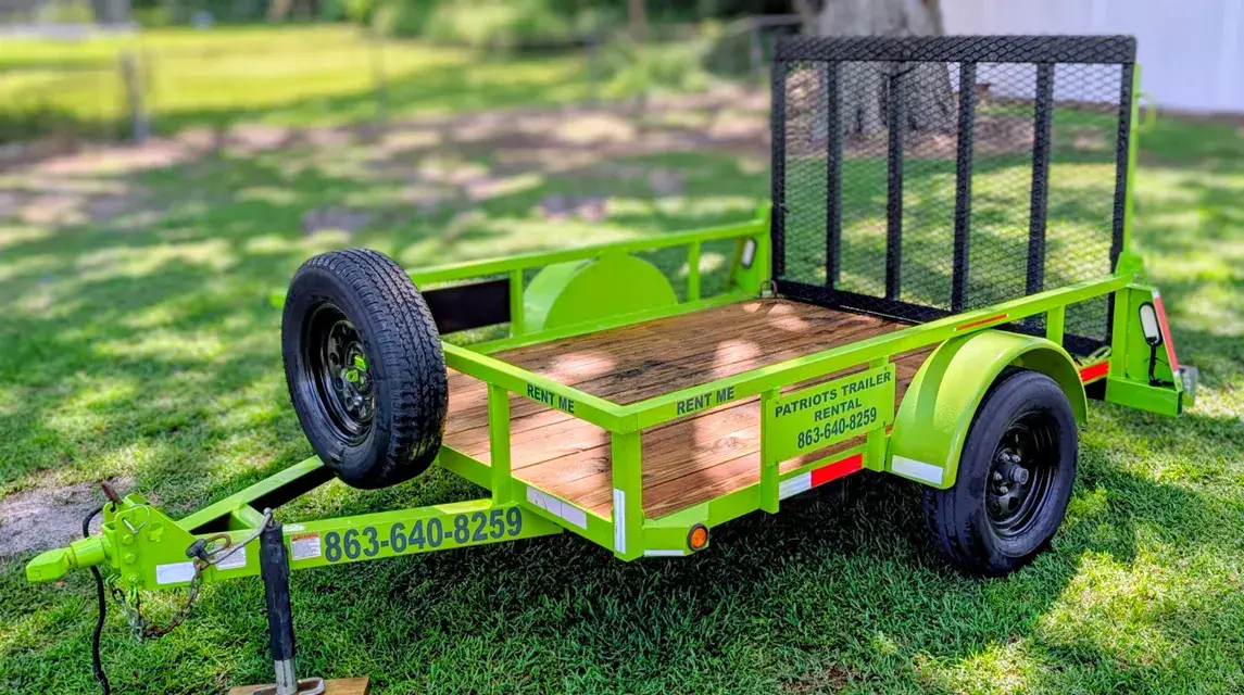 Green trailer with spare tire, 863-640-8210, on grass, Patriots Trailer Rentals.