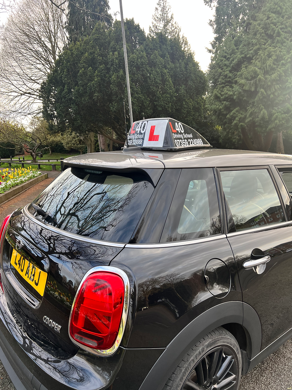 rear three-quarter view of a black MINI driving school car with roof sign and license plate L40 ABJ, park background, tall landscape