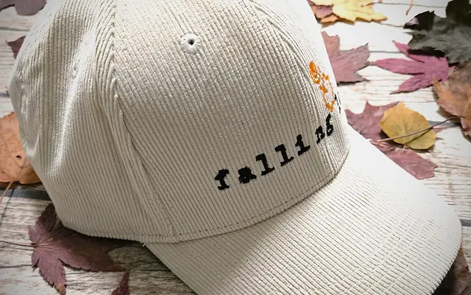 A sand coloured cap with organic cotton corduroy texture, embroidered in black with "falling leaf" and the orange falling leaf logo