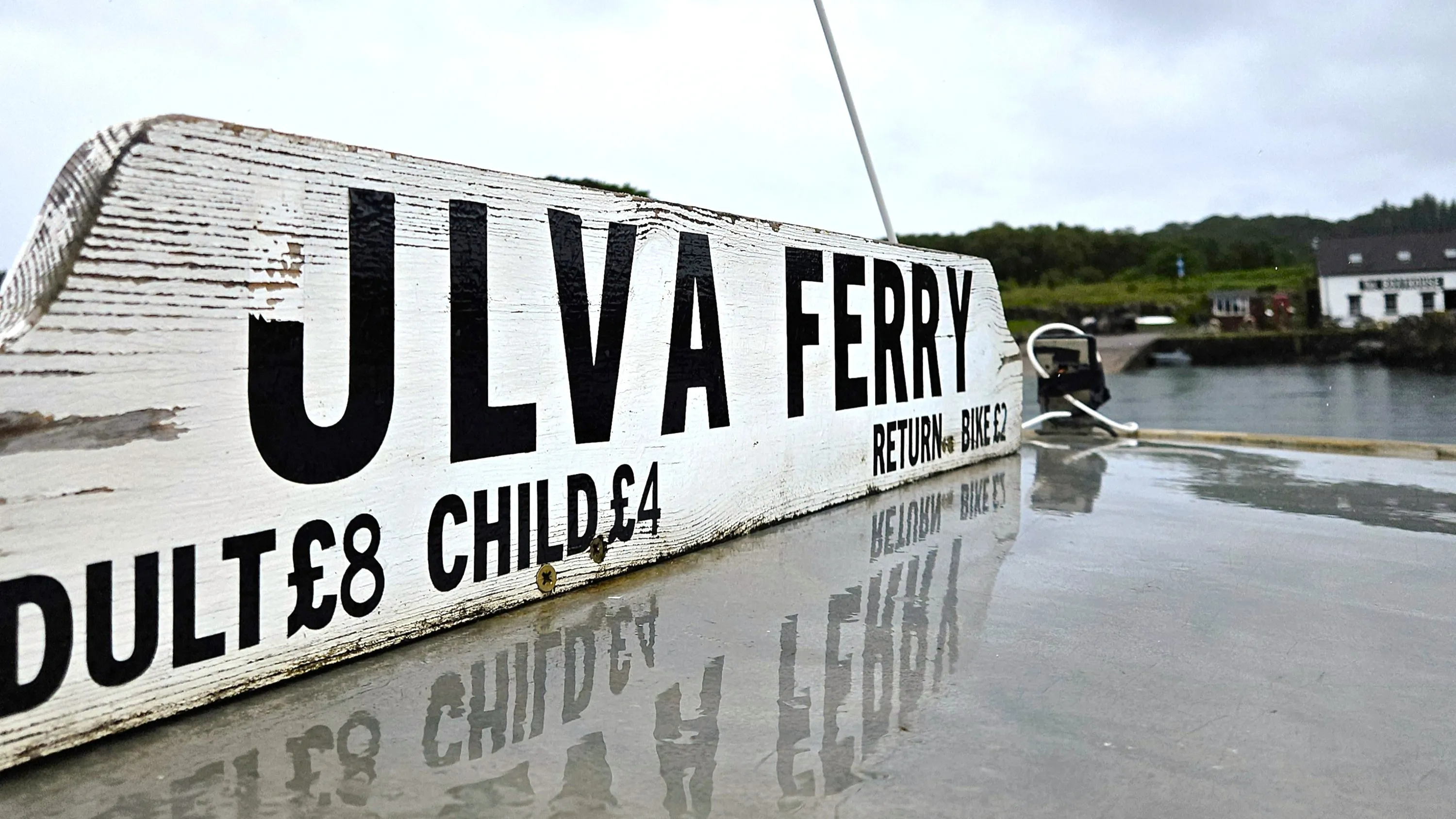 A view of the top of the Ulva Ferry, with a white sign on it with black writing stating Ulva Ferry and the prices, £8 for adults and £4 for children return, bikes £2.