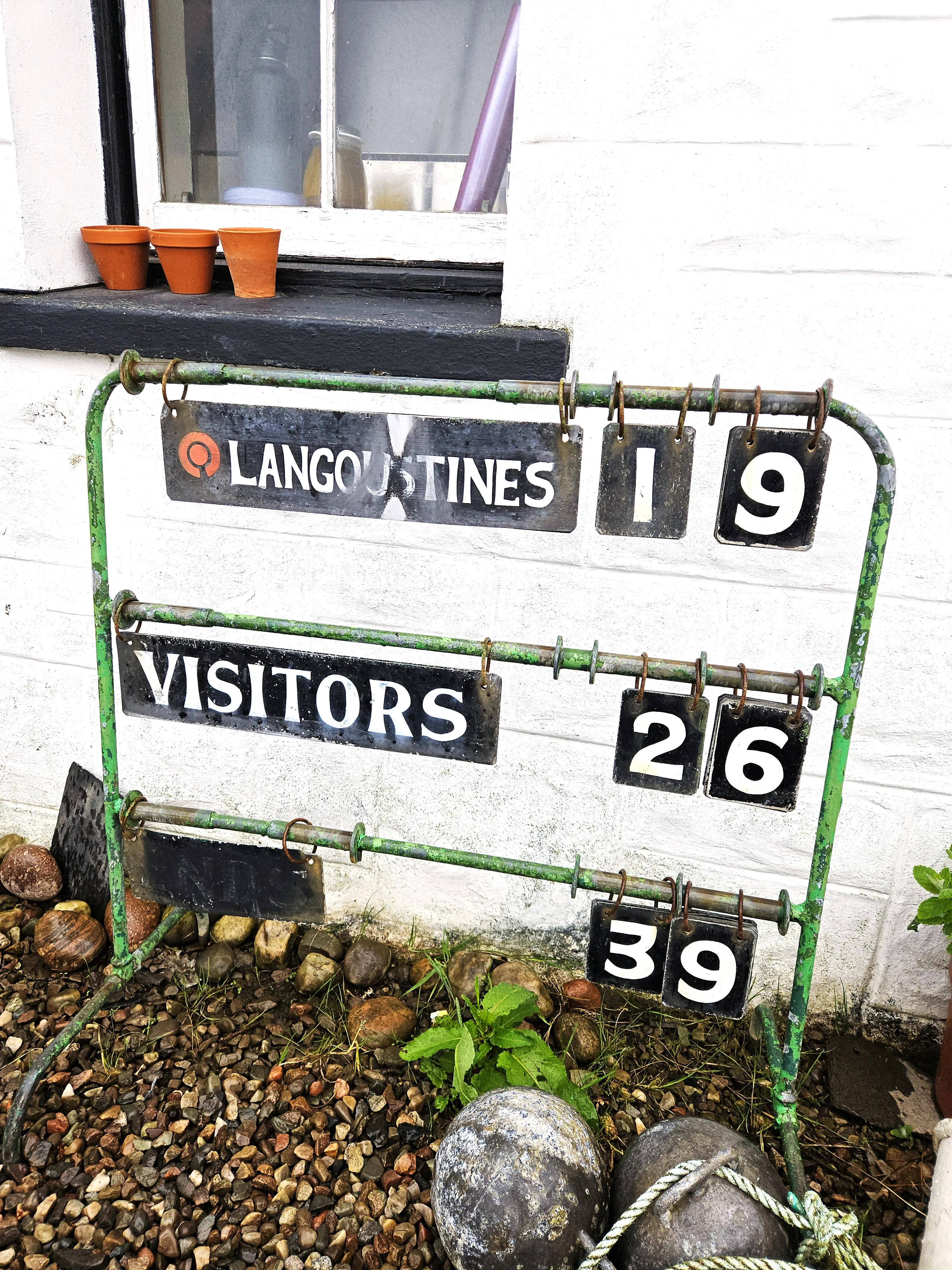 A rustic counter sign outside The Boathouse stating "langoustines - 19, visitors 26" it also has the number 39 but no explanation of what this count is of. 