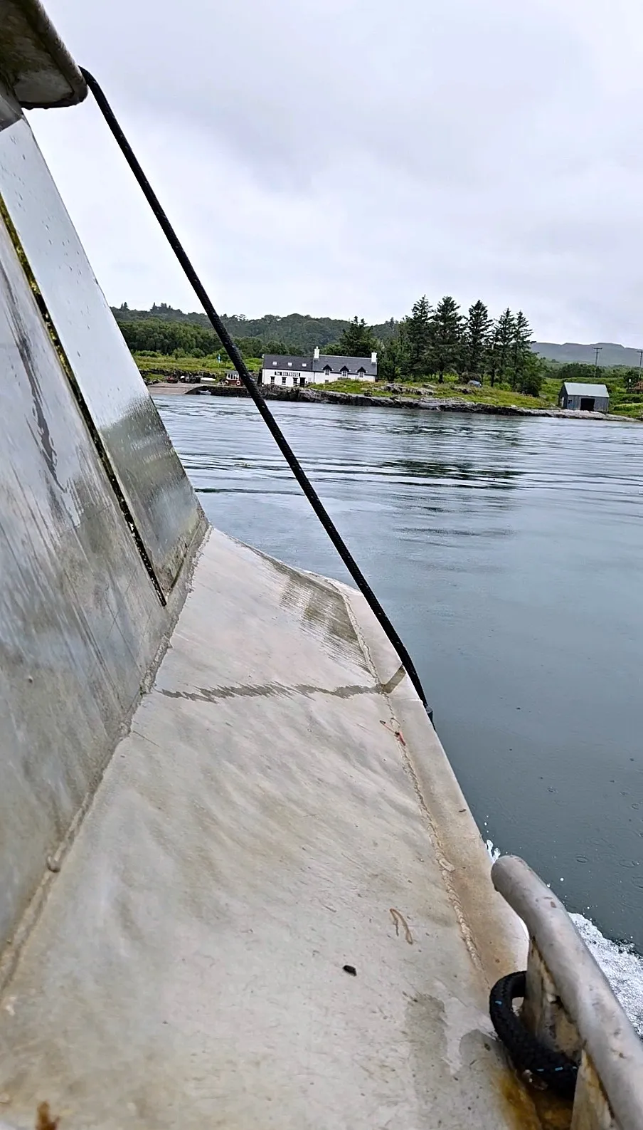 A view from the Ulva ferry across to The Boathouse, with calm waters and trees surrounding the white building.