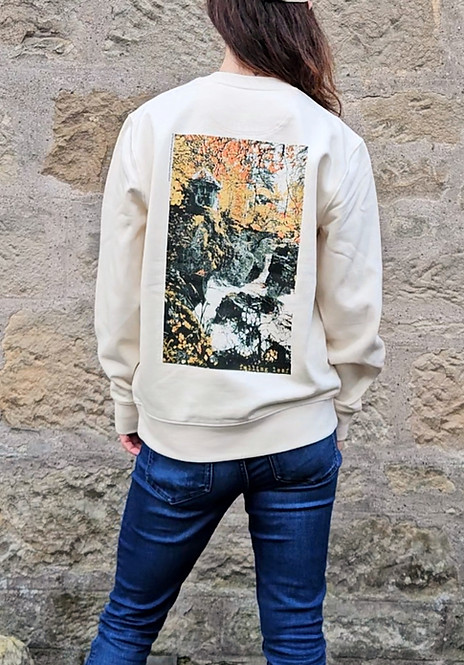 A woman wearing a cream sweatshirt with a waterfall print (the Hermitage in Perthshire) on the back, and blue jeans