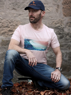 Man crouched like a superhero wearing the pink Mill Bay organic cotton t-shirt with stonewash jeans