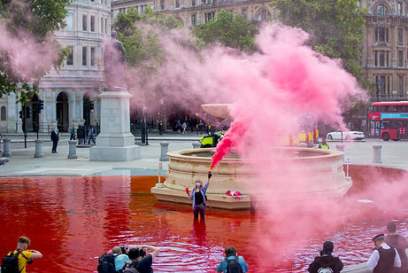A woman standing in a fountain dyed red holding, with pink smoke all around