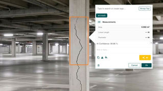 Concrete parking garage pillar with a long vertical crack highlighted in orange and an AI measurement popup showing ai-crack.