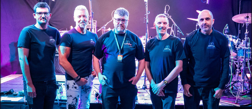 a group standing in front of drums at a music venue