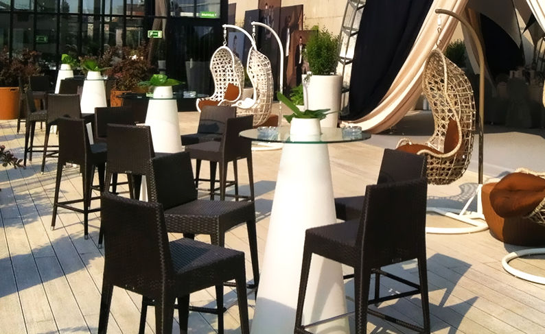 Terrasse moderne avec tables hautes, tabourets et chaises suspendues design.