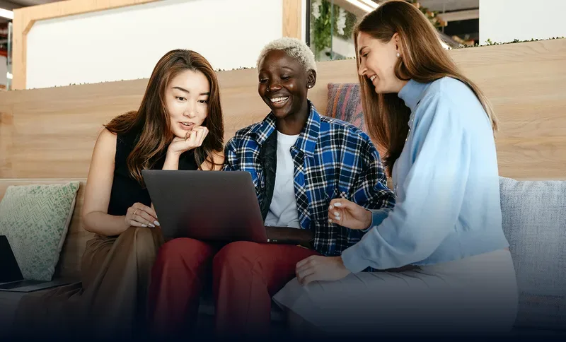 Drei Kolleginnen schauen gemeinsam auf einen Laptop