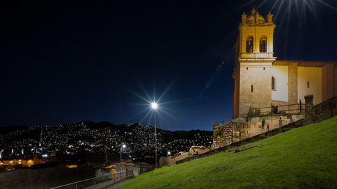San Cristóbal Church bell tower illuminated from above at blue hour, overlooking Cusco with a lone streetlamp in the foreground