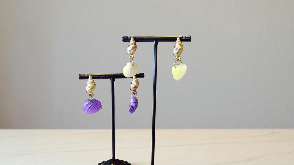 Delicately crafted, The Seashell Earrings feature a small seashell in lilac or yellow on a gold-toned shell. These petite ear