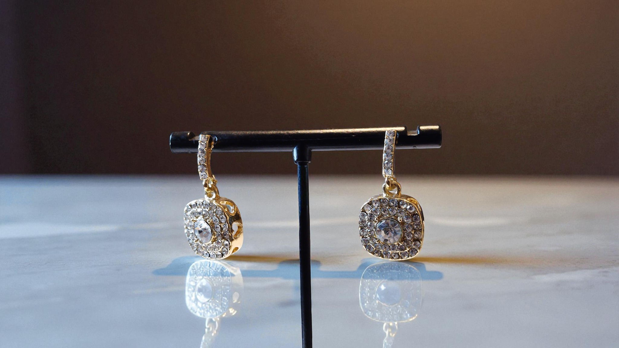 Discover The Naomi Bezel Earrings, a stunning addition to any collection. In a bezel shape with rhinestones set in a gold ton