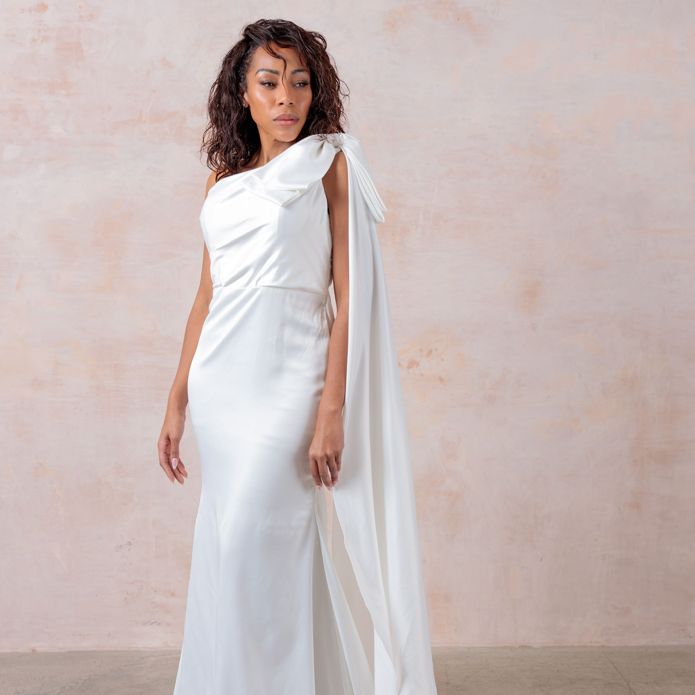 A one-shoulder ivory satin wedding gown with a flowing bow train adds elegance and timelessness.