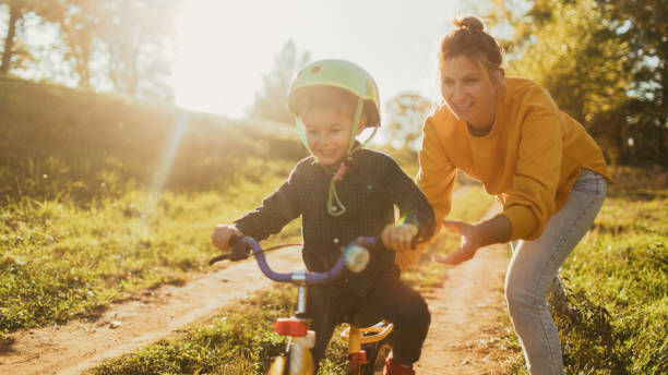 Photo of a young boy who is learning to ride a bicycle with a little help from his mother.