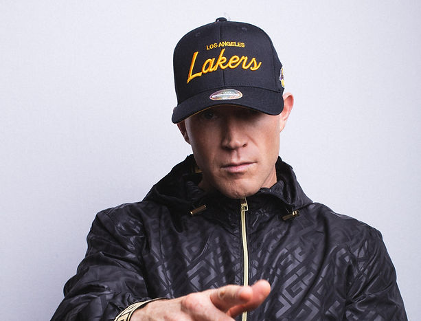 Man wearing lakers cap and black jacket in white background.