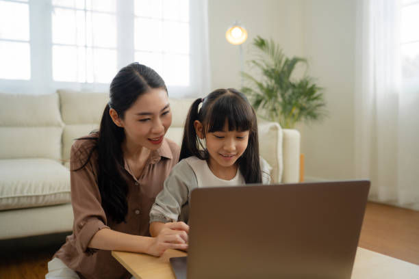 Mother teaching daughter do homework by using tablet device for homeschooling.