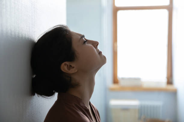 Tired stressed indian woman sit leaning against white wall in light room try to cope with problems. Side profile view of young lady face with closed eyes think breath deep