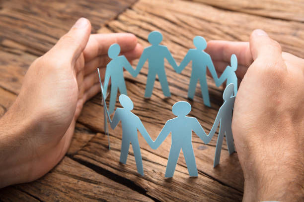 Businessman's Hands Covering Paper Team on wooden table.