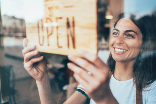 Portrait of a happy business owner hanging an open sign on the door at a cafe and smiling.