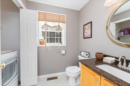 Small bathroom features toilet, wood vanity, sink, mirror, and laundry unit.