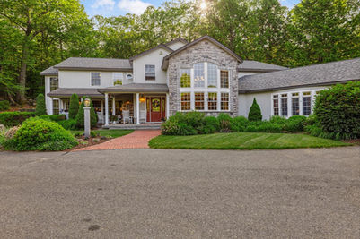 Elegant large house with stone facade, red door, and lush trees.